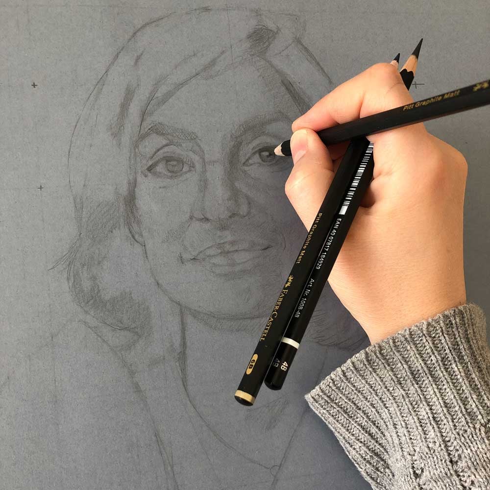 Photo de main en train de dessiner un portrait au crayon